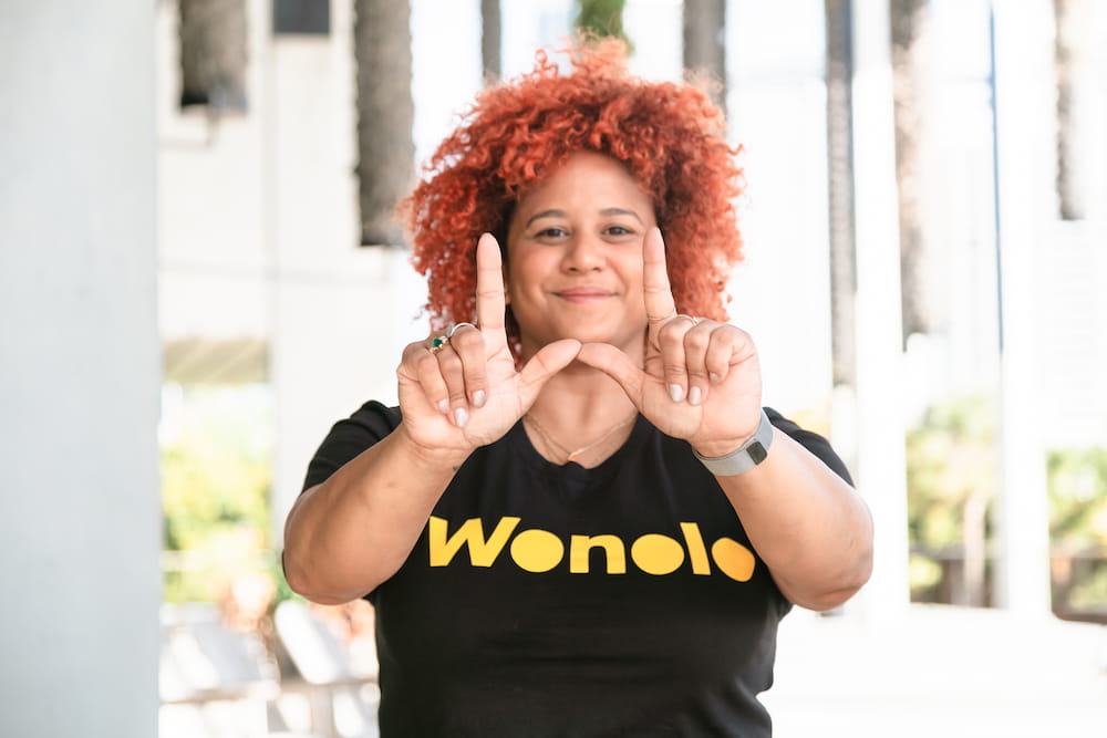 A person wearing a Wonolo shirt makes a W with their hands while working a gig economy job.