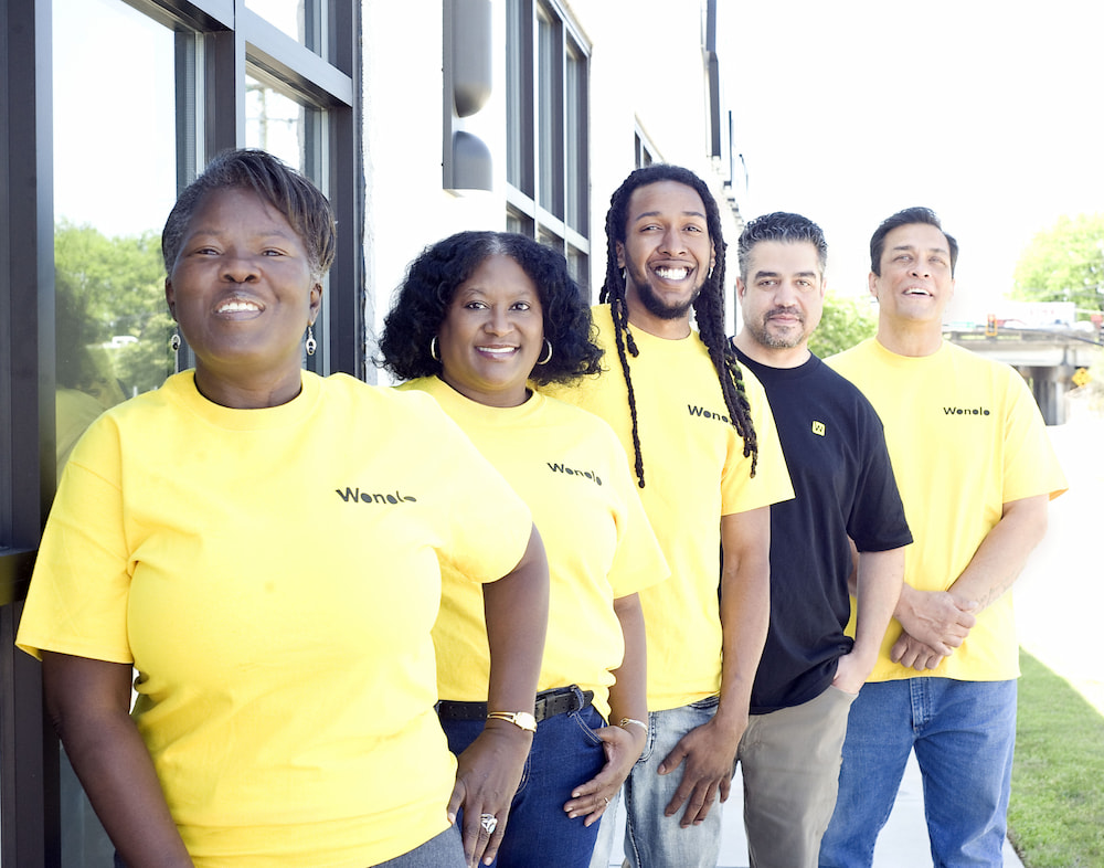 A group of freelancers wearing Wonolo shirts stand in front of a building down town while getting ready for their next side jobs.