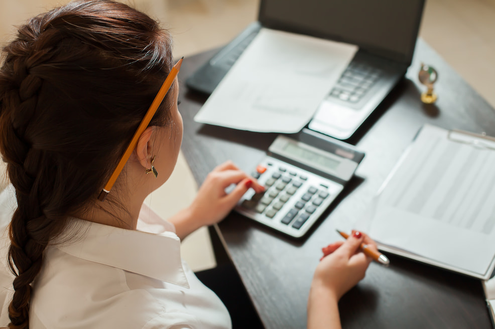 A bookkeeper sits at a desk with a laptop and calculator while balancing numbers.