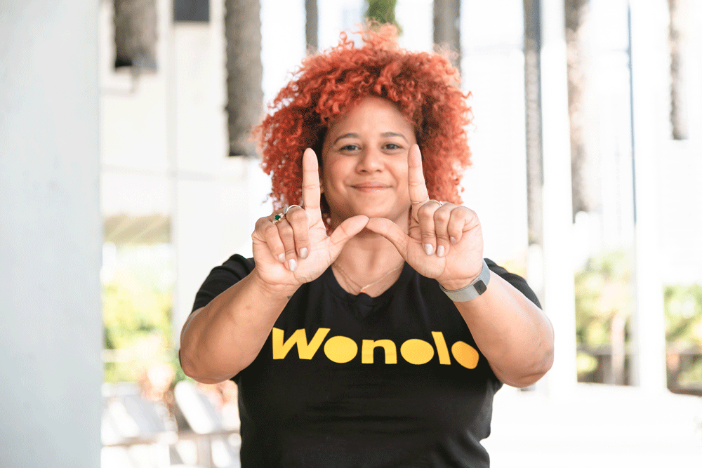 A person in a black shirt that says Wonolo in yellow holds up their hands in the shape of a W.