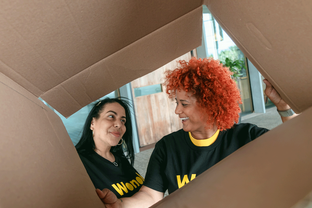 Two retail workers pack boxes while wearing Wonolo shirts.